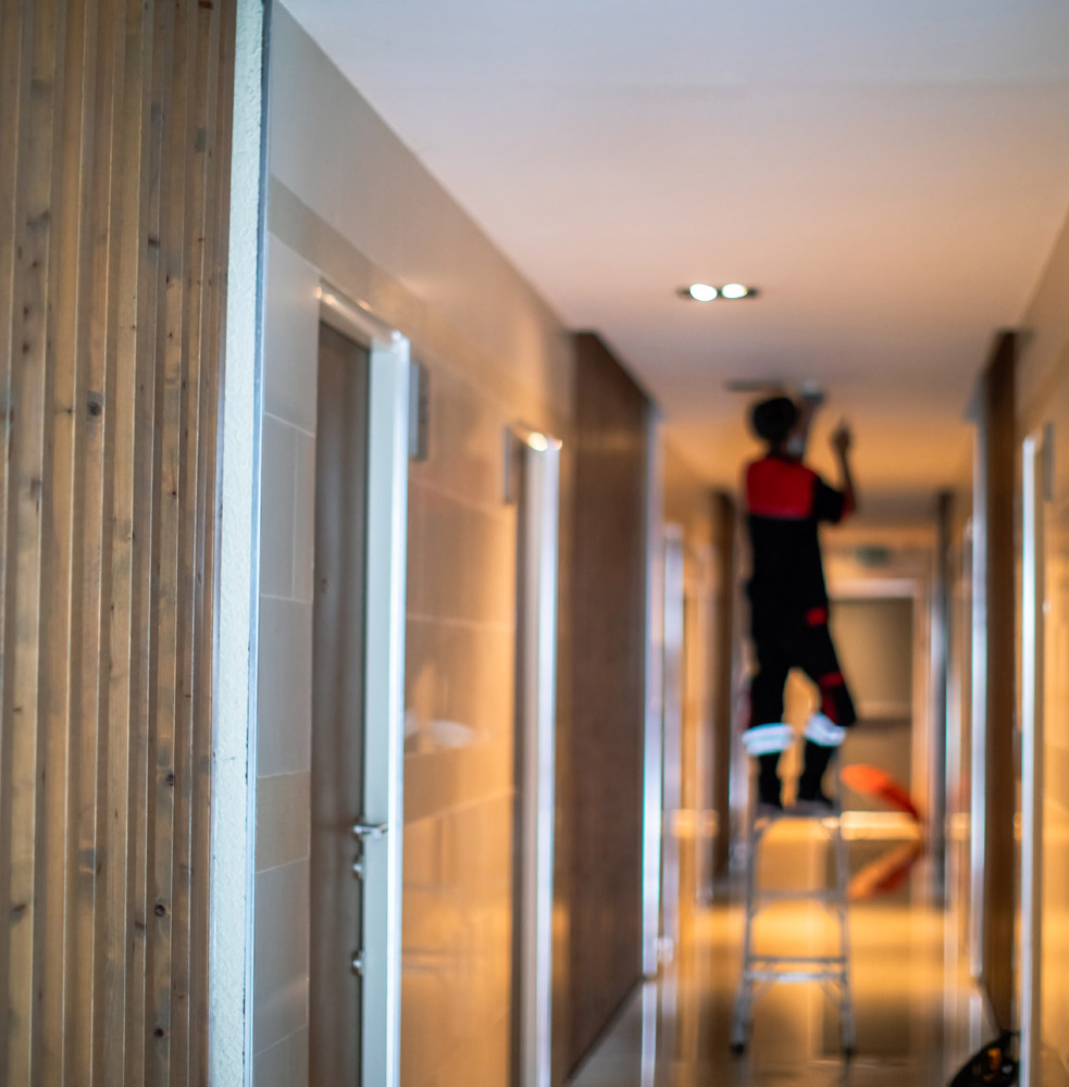 Man standing on ladder installing and testing fire alarm
